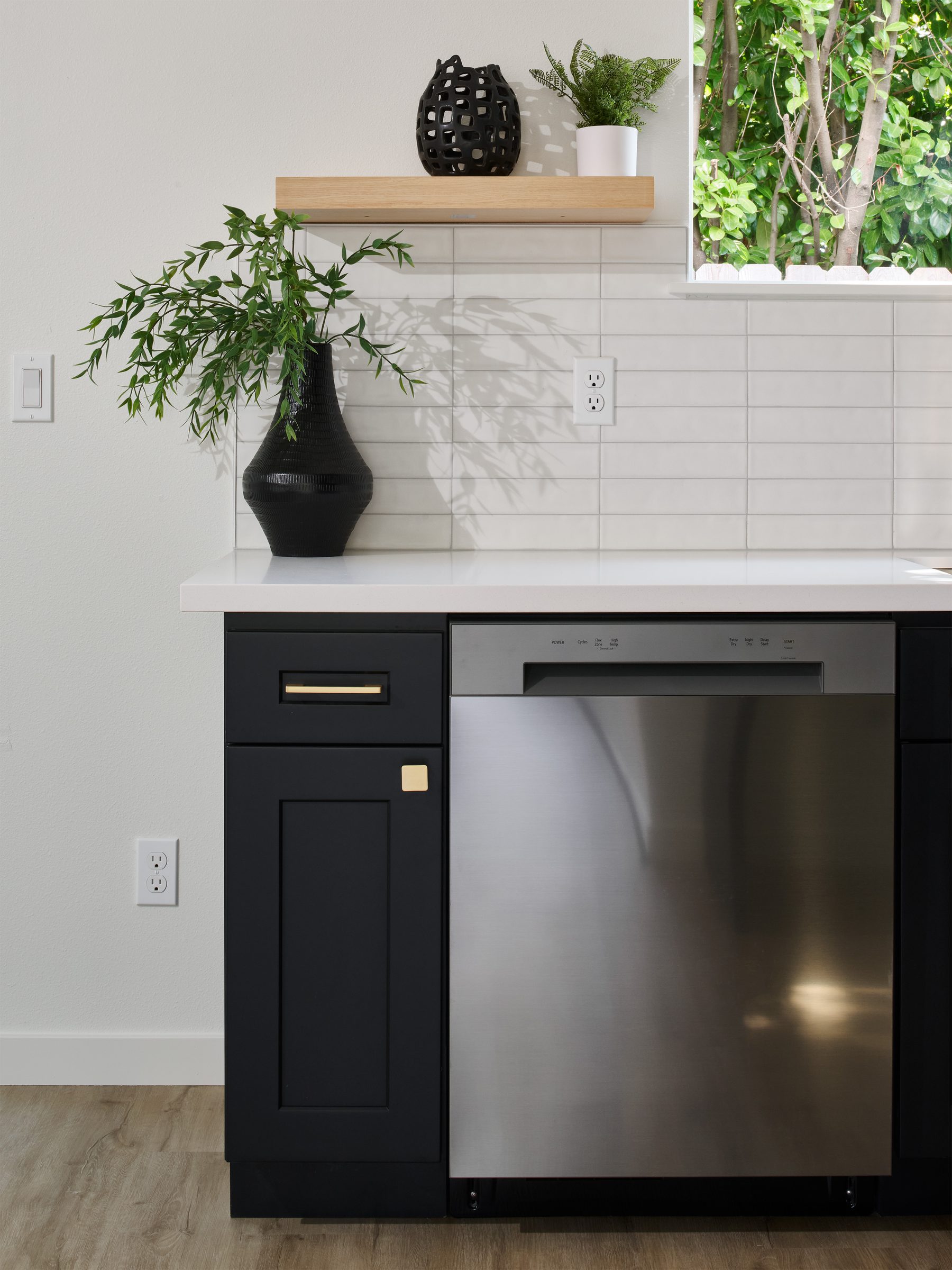 Kitchen detail: black cabinetry, stainless dishwasher, and brass pull